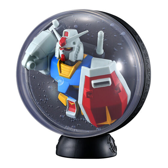 ガンダム：白い頭部と青い胸、赤い盾を前へ出した姿。背面には細かな凹凸の背景があります。